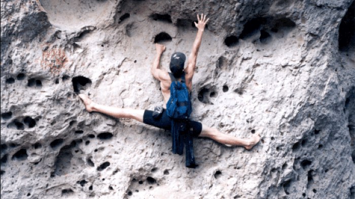 Rick Tew holding the full splits across a cliff face while climbing